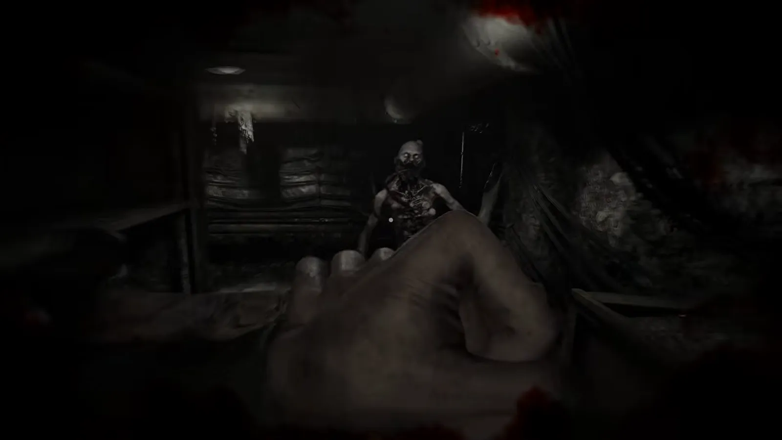 Humanoid figure approaching in a dim room beyond the player raised hand silhouette in foreground